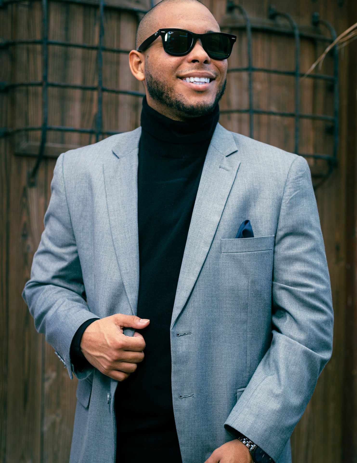 a man in a suit and sunglasses standing in front of a fence